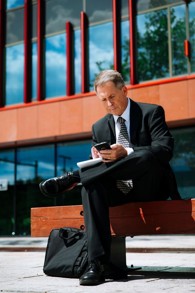 International debt collection: Raymond Pappot sits on a bench looking at his smartphone.