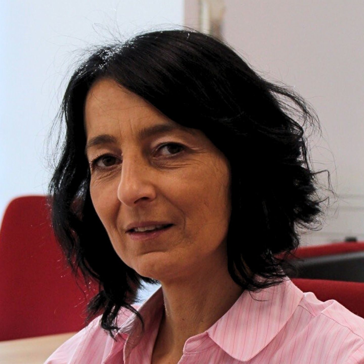 Cristina Pasere, Manager of Compliance Operations Support at EOS Romania, is sitting at her desk in a pink striped blouse and looking at the camera.