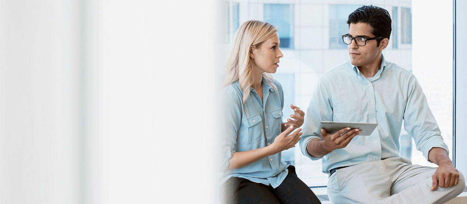 Two young people talking and looking at a tablet.