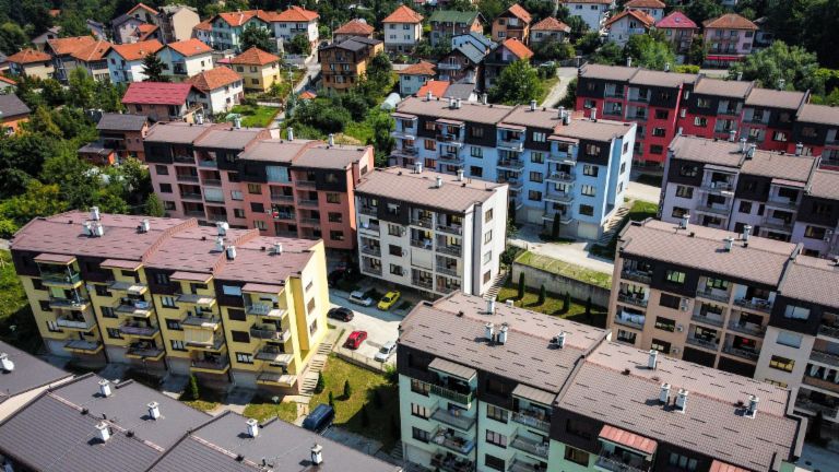 An aerial view highlights a vibrant residential complex featuring numerous multi-colored apartment buildings amidst green surroundings in Bosnia.