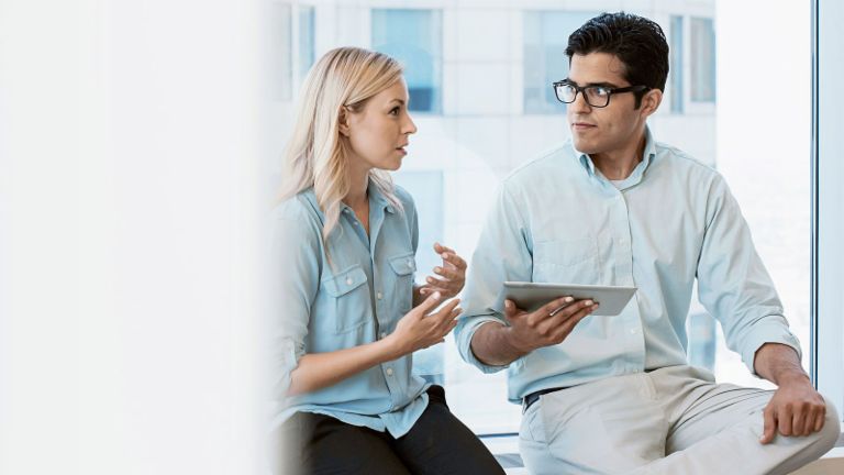 Two young people talking and looking at a tablet.