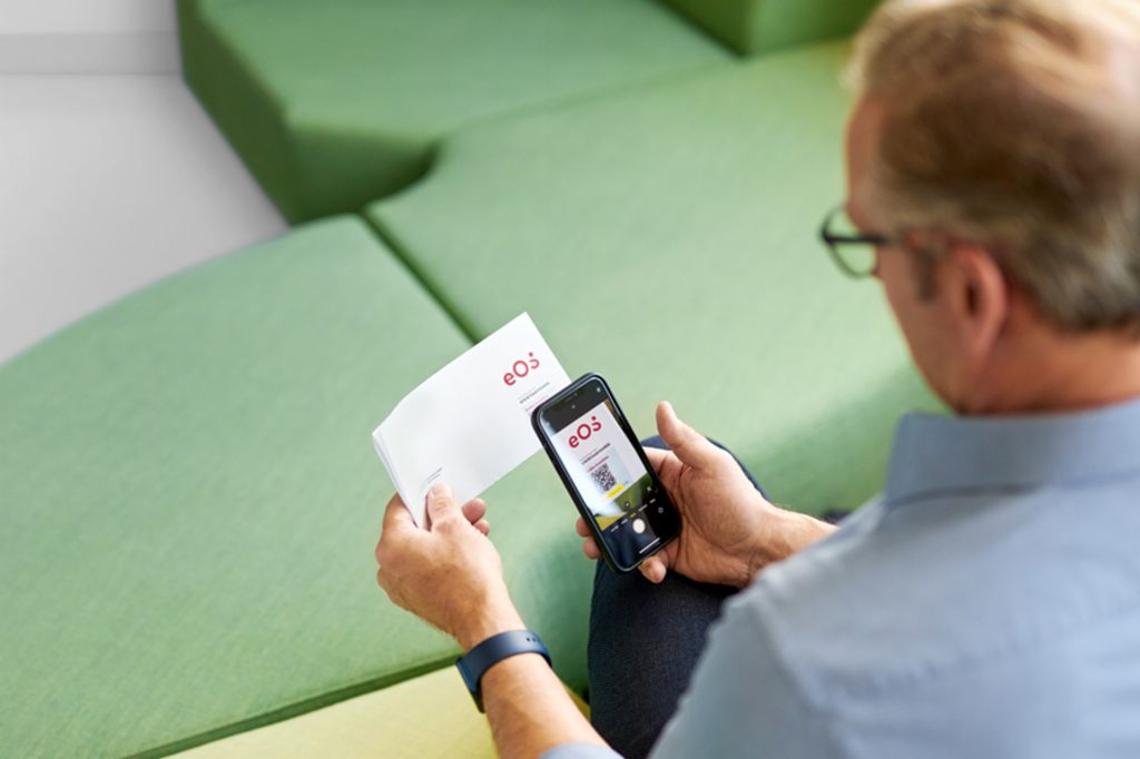 A man scans a QR code on a letter from EOS with his smartphone to settle his open claim online on the EOS Portal.