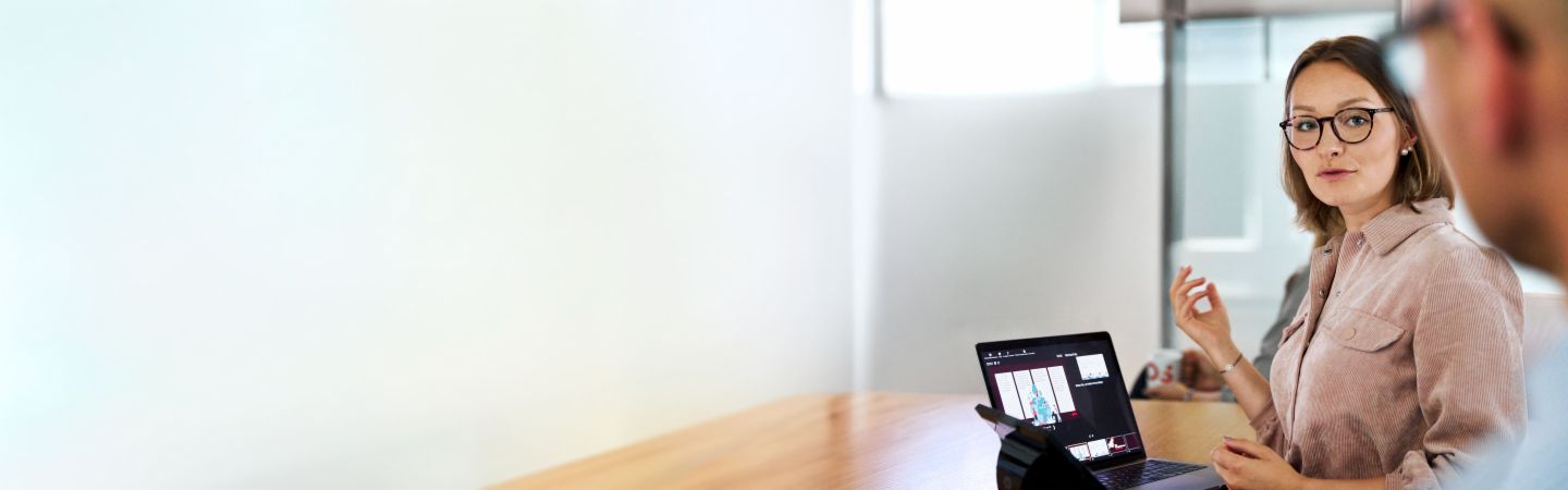 EOS employee with glasses presenting on a laptop during a meeting, illustrating the EOS Group's corporate responsibility commitment.