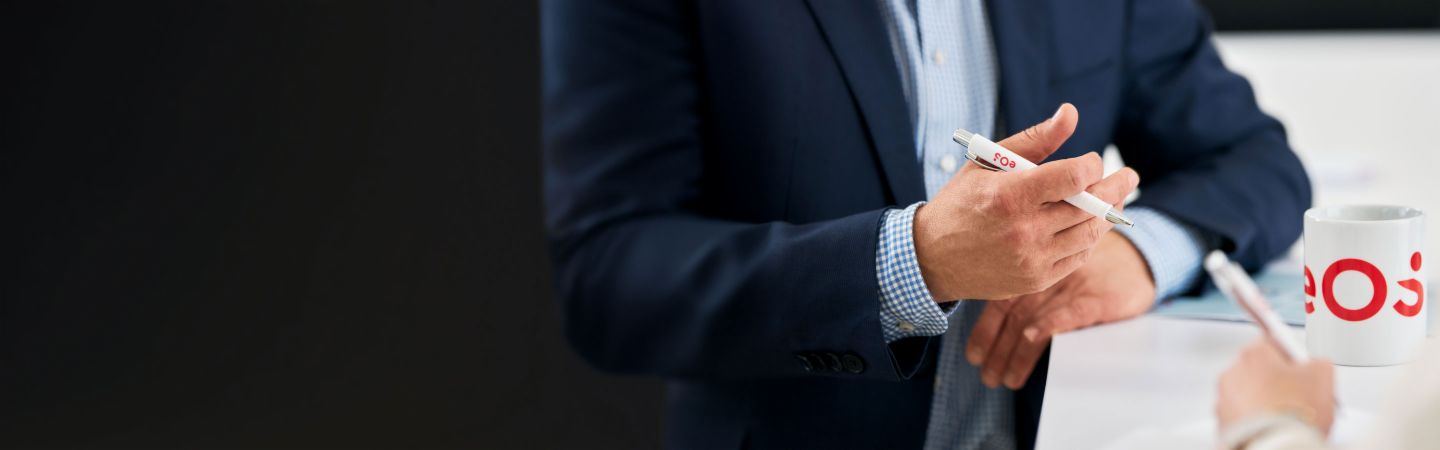 Section Stage About us Businessman holding EOS pen during a conversation about international receivables management, EOS cup on the table - Expertise in debt collection, NPLs, and digital solutions