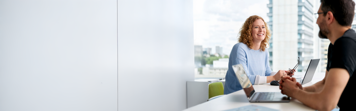 Two EOS employees are working with laptops in a modern office with large windows in the background.