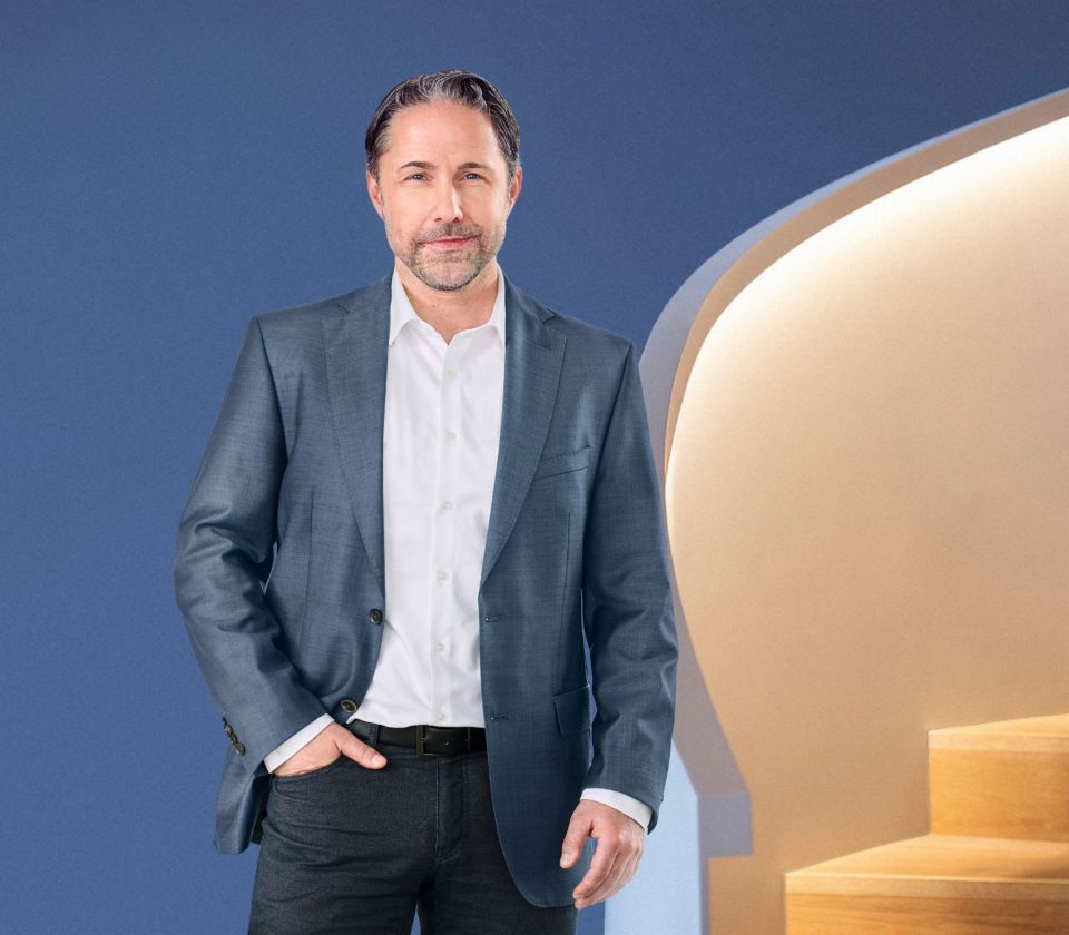 Marwin Ramcke, CEO of the EOS Group, stands against a blue background and wears a dark jacket.
