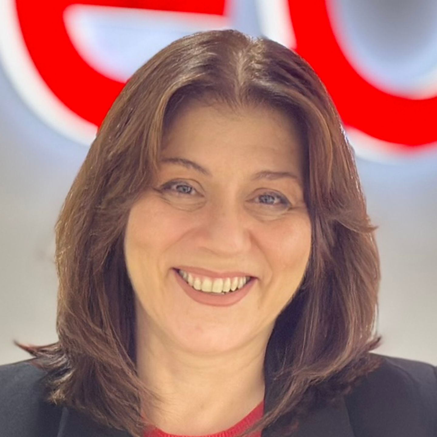 Belén Barreiro, Contact Center Agent at EOS in Spain, is leaning against a counter in a black blazer in front of a bright EOS logo.