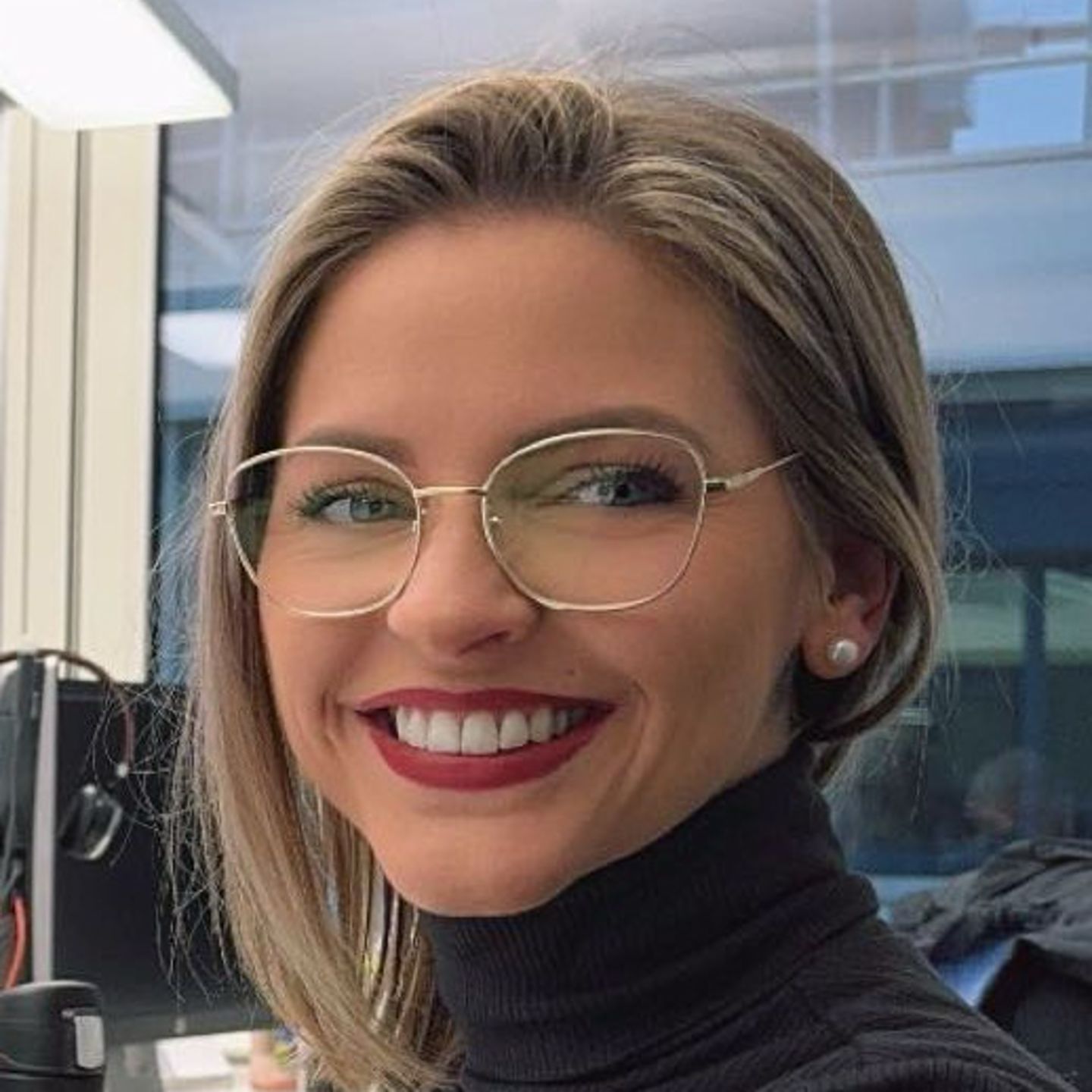 Genny Bollinger, Debt Restructuring Specialist at EOS in Switzerland, is sitting at her desk in a gray turtleneck sweater and smiling at the camera.