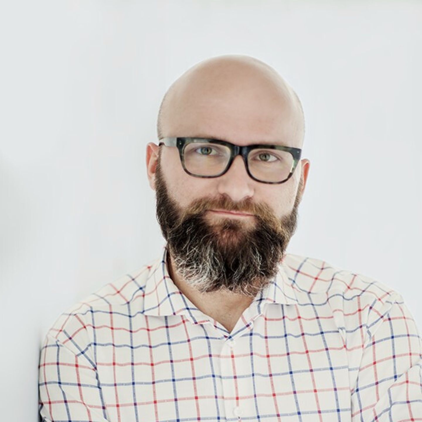 Dr hab. Tomasz Piekot with a plaid button-down shirt leaning against a white wall