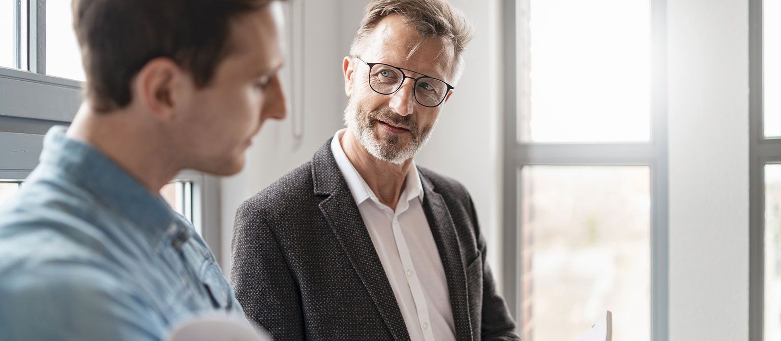 Two men in an office are discussing the results of the EOS Group's European Payment Practices 2025 study on digitization in receivables management.