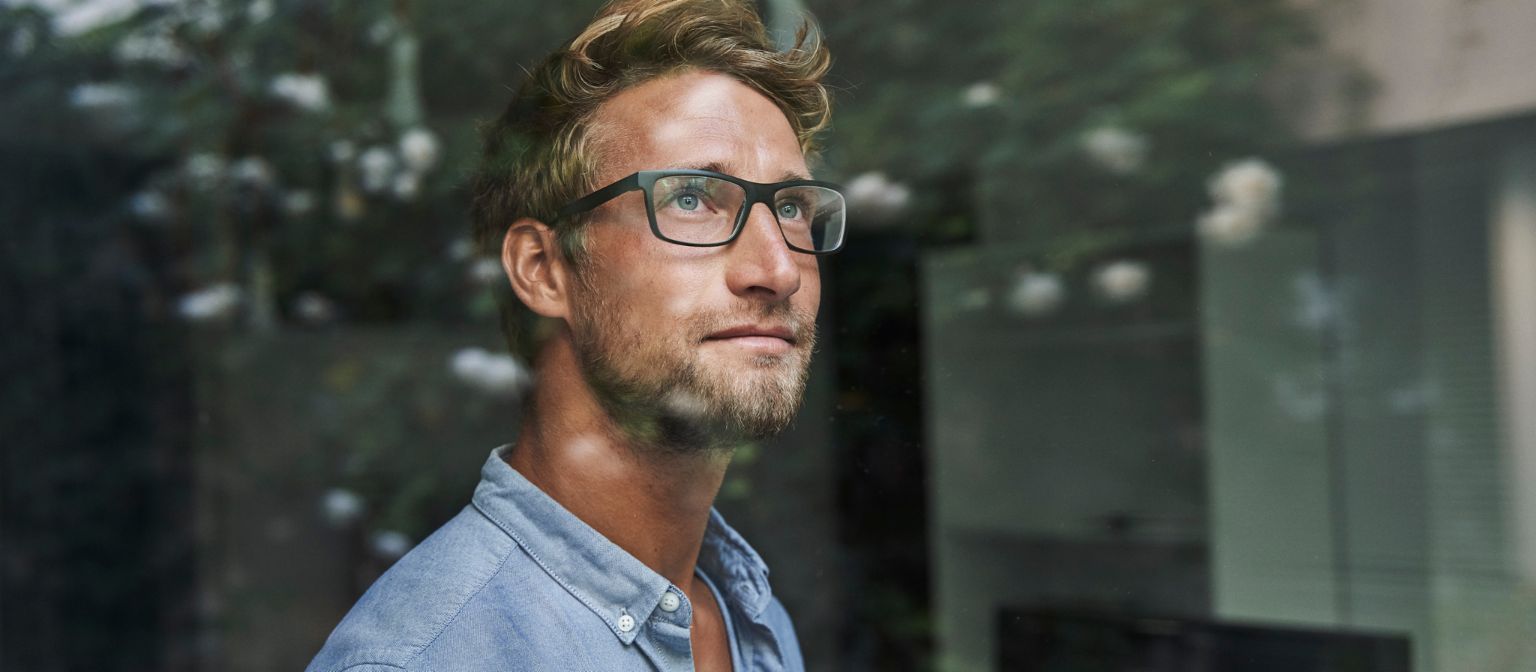 A young Gen Z man peers anxiously out the window.