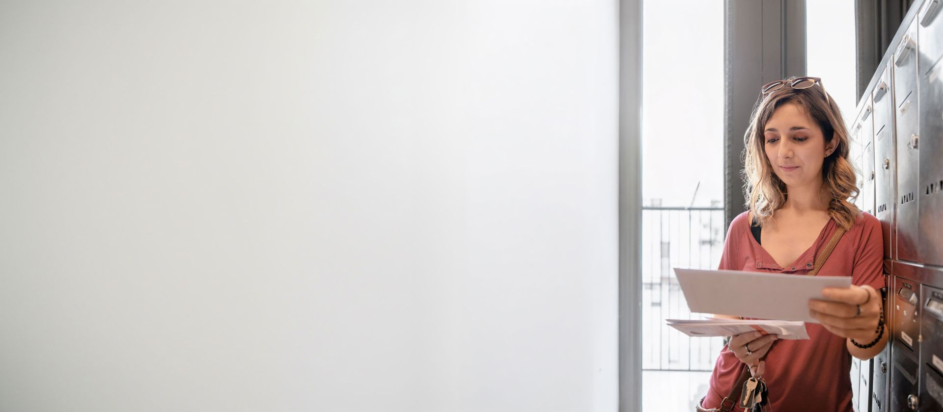 Woman standing in the hallway in front of the letter boxes, reading a letter she just opened.