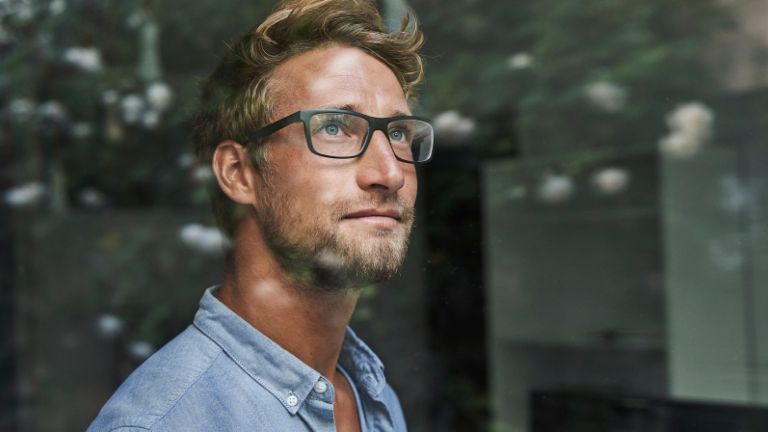 A young Gen Z man peers anxiously out the window.