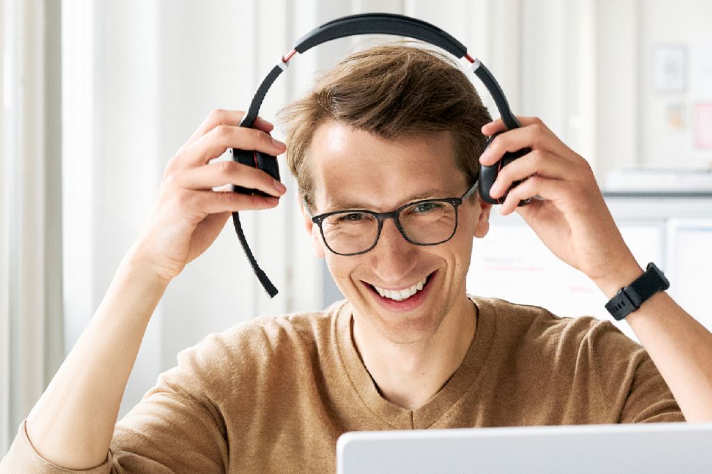 Jung man sitting at a desk and smiling into the camera while putting on his headphone